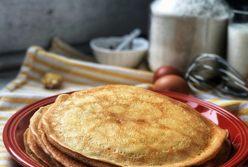 Pile de pancakes protéinés maison dorés sur assiette rouge avec ingrédients farine lait œufs fouet, recette 100% Dragon Nutrition spéculoos