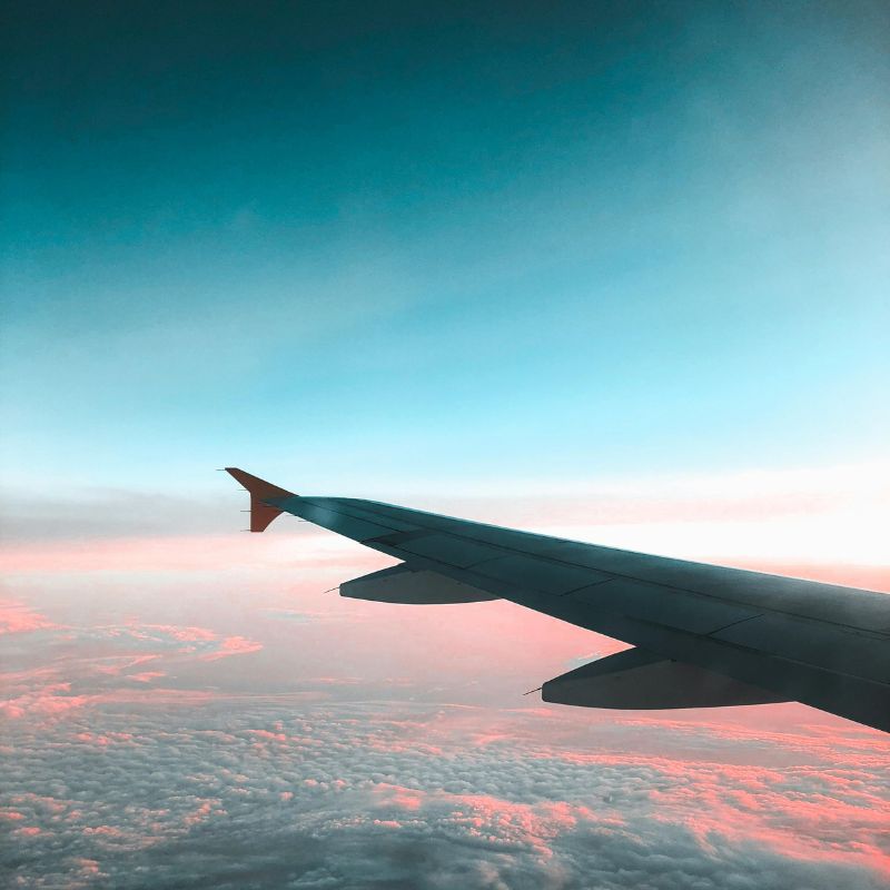Aile d'avion traversant des nuages au coucher du soleil, vue aérienne depuis le cockpit avec ciel bleu et rose
