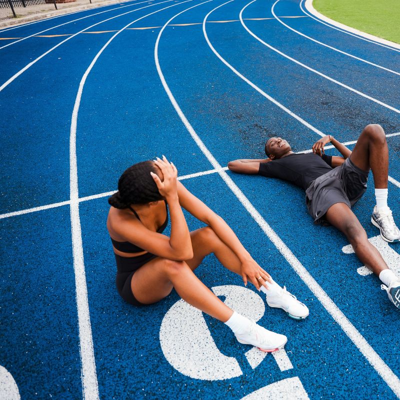 Athlètes épuisés sur piste d'athlétisme après entraînement intense, fatigue due à carence fer, importance supplémentation et aliments riches pour sportifs Dragon Nutrition
