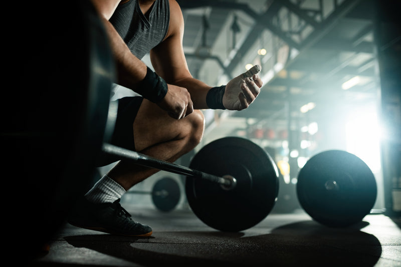 Homme musclé accroupi en train de se préparer à soulever une barre lourde dans une salle de musculation