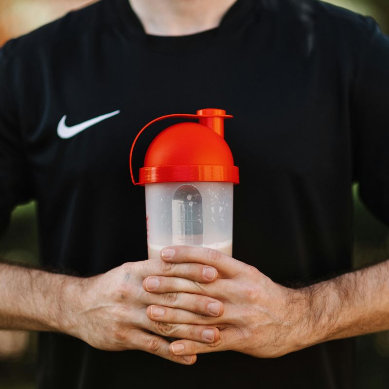 Homme en t-shirt Nike noir tenant un shaker rouge rempli de boisson protéinée, en extérieur