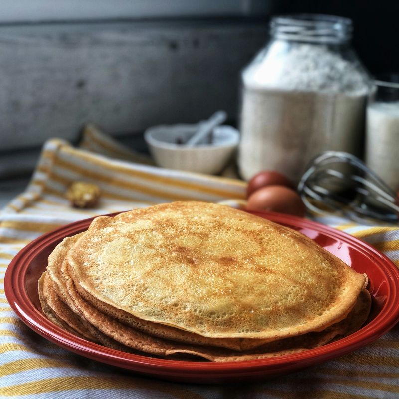 Pile de pancakes protéinés maison dorés sur assiette rouge avec ingrédients farine lait œufs fouet, recette 100% Dragon Nutrition spéculoos