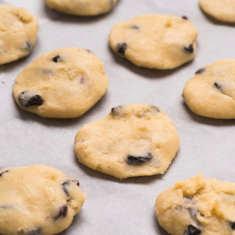 Pâte à cookies aux pépites de chocolat disposée en petits tas sur une plaque recouverte de papier cuisson avant la cuisson