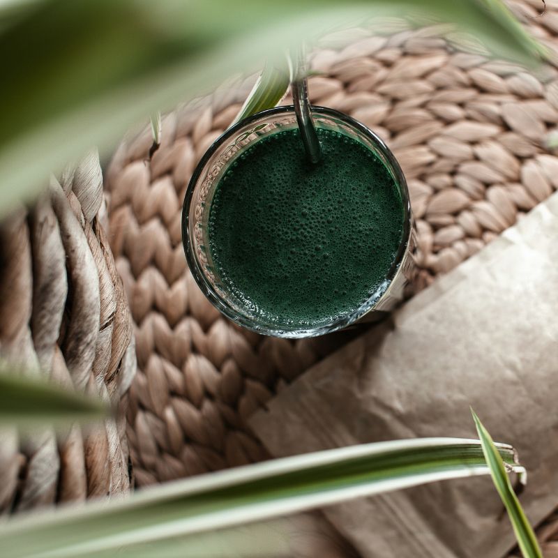 Smoothie vert spiruline dans verre avec sachet poudre à côté sur setosier, meilleure source fer végétal pour sportifs vegan endurance musculation