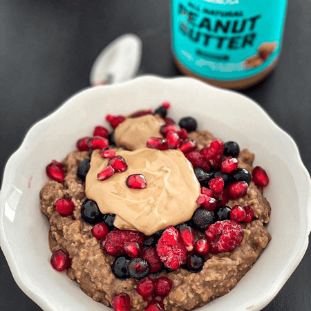Bol de porridge garni de beurre de cacahuète BioTechUSA et de fruits rouges avec le pot turquoise flou en arrière-plan