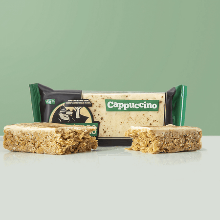 Barre flapjack Blackfriars saveur cappuccino, enrobée d’un glaçage crème, présentée coupée devant l’emballage vert et noir sur fond vert pastel