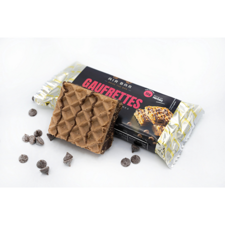 Gaufrette protéinée chocolat Air Bar posée devant son emballage avec éclats de pépites de chocolat autour, montrant les couches au cacao