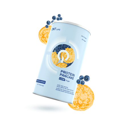 Boîte cylindrique QNT Protein Pancake low sugar goût myrtille entourée de pancakes dorés et de myrtilles fraîches sur fond blanc