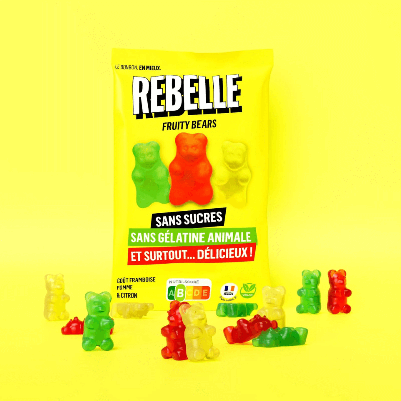 Sachet jaune de bonbons Rebelle Fruity Bears sans sucres ni gélatine animale entouré d’oursons gélifiés rouges, verts et jaunes sur fond jaune