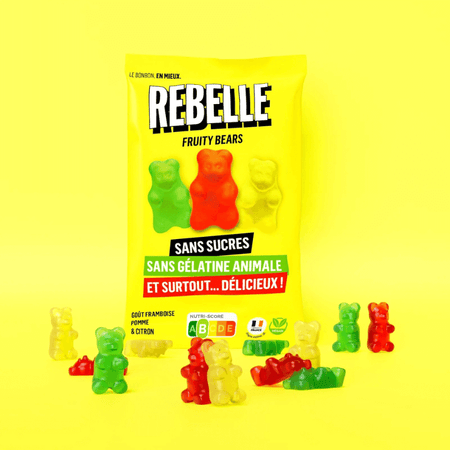 Sachet jaune de bonbons Rebelle Fruity Bears sans sucres ni gélatine animale entouré d’oursons gélifiés rouges, verts et jaunes sur fond jaune
