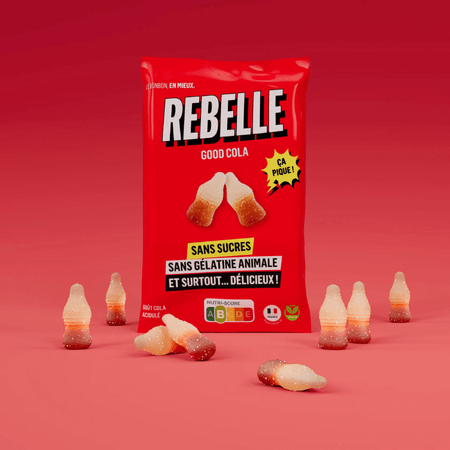 Sachet rouge de bonbons Rebelle Good Cola sans sucres ni gélatine animale entouré de bonbons en forme de bouteille sur fond rouge