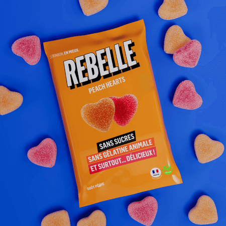 Sachet orange de bonbons Rebelle Peach Hearts sans sucres ni gélatine animale entouré de cœurs gélifiés goût pêche sur fond bleu vif