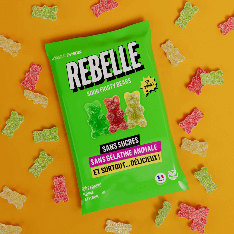 Sachet vert de bonbons Rebelle Sour Fruity Bears sans sucres ni gélatine animale entouré d’oursons gélifiés acidulés rouges, verts et jaunes sur fond orange