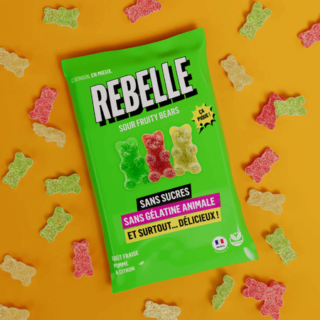 Sachet vert de bonbons Rebelle Sour Fruity Bears sans sucres ni gélatine animale entouré d’oursons gélifiés acidulés rouges, verts et jaunes sur fond orange